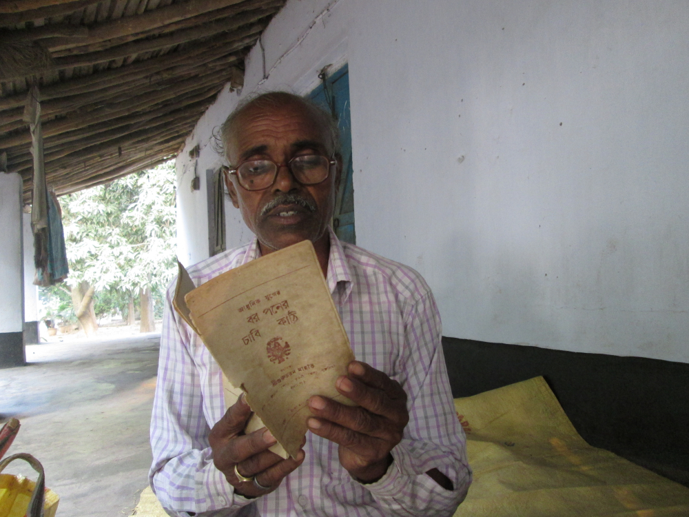 চিত্র ৫. বলরামপুরের ‘রয়্যাল ছৌ অ্যাকাডেমি’তে রুচাপ গ্রামের স্থানীয় ঝুমুর শিল্পী গুরুচরণ মাহাত। তাঁর হাতে তাঁরই লেখা একটি ঝুমুর গানের সংকলন ‘আধুনিক যুগের বর পনের চাবিকাঠি’। গুরুচরণ মাহাত পেশায় কৃষিজীবী। তাঁর ঘোড়ানৃত্যের দল রয়েছে। দলের সম্মুখভাগে দুটি ঘোড়ার উপর নাচিয়েরা নাচেন বলে এই নাচকে ঘোড়ানৃত্য বলে। ঝুমুরের তালেই হয় এই নাচ। ঝুমুর ছাড়াও অহিরা ও টুসু গানও লিখে থাকেন গুরুচরণ। (সৌজন্যে: সোহম দাস)