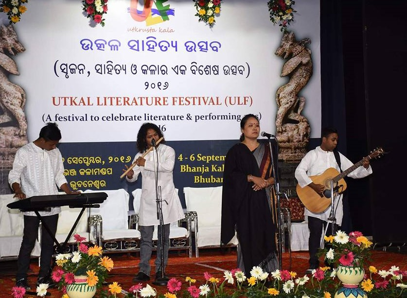 Fig. 2. Pavitra Lama performing avisangi kavita at Utkal Literature Festival, Bhanja Kala Mandap, Bhubaneswar, Orissa on September 4, 2016. Her performance is accompanied by live music played by the band Dhoka Aghi Mrityu Parkhandai. Lama’s black shawl is part of the costume and marks her protest against child labour (Courtesy: Ganesh Sahoo)