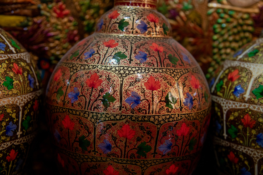 Vibrant hues of gold, red, and turquoise, made from natural pigments, enhance the floral and arabesque patterns adorning these papier-mâché artifacts. 