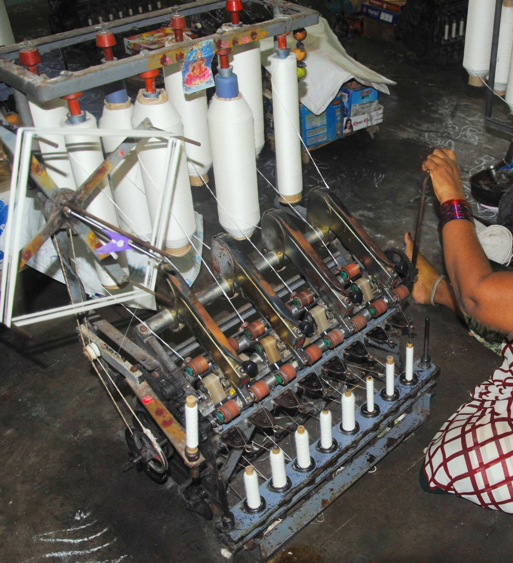 Ambar charkha with the crank used to operate it (right). The roving at the top pushes the slightly twisted thicker yarn through the rollers in between. 