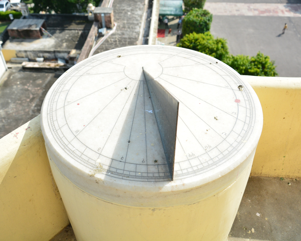Fig. 5: A small dhoopghadi mounted on a custom-made pillar on the southern railing of the City Palace ghanta ghar balcony sports lines and Dhundari numbers on its top surface and a copper alloy gnomon