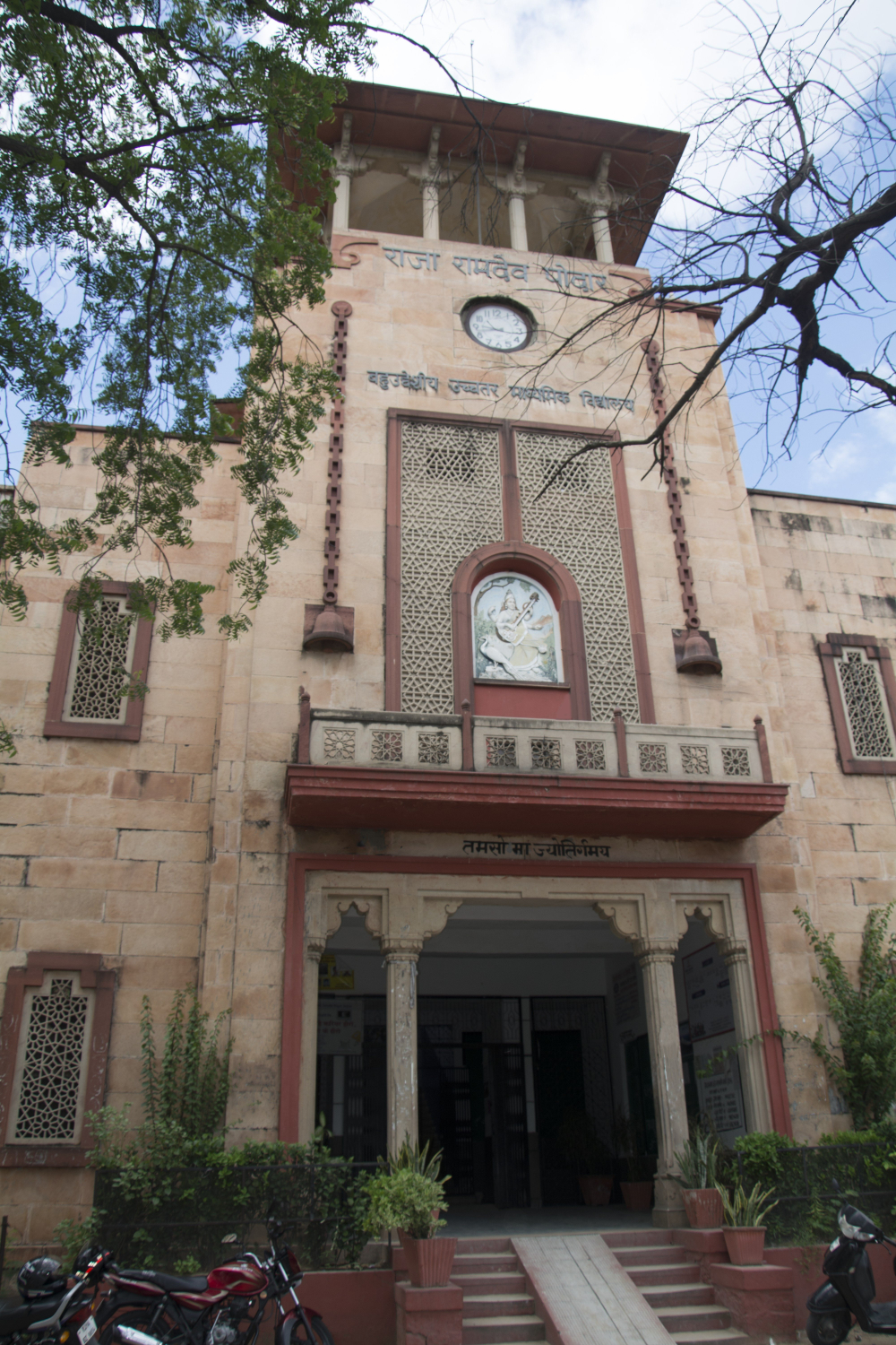 Fig. 8: The tower clock at Raja Ramdev Poddar School occupies a hole in the building facade with two chained bells set in stone on either side of the clock face