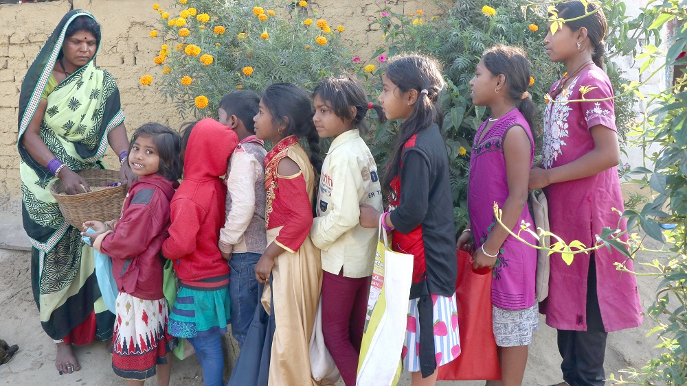 Children lined up in front of a house to receive grains