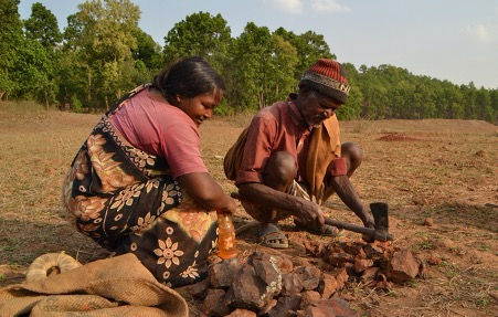 चित्र  1. पोलपोल पाट गाँव के बिरेश्वर असुर लौह पत्थरों के टुकड़े करते हुए। साथ में सखुआपानी गाँव की सुषमा असुर। (फोटो: विजय गुप्ता, सखुआपानी, नेतरहाट, 14 मई 2013)